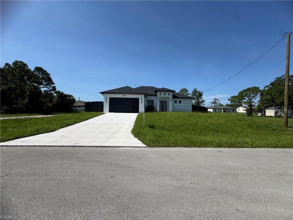 A single-story house with a dark garage door and a concrete driveway under a blue sky — 3901 3RD STREET SW, LEHIGH ACRES, FL