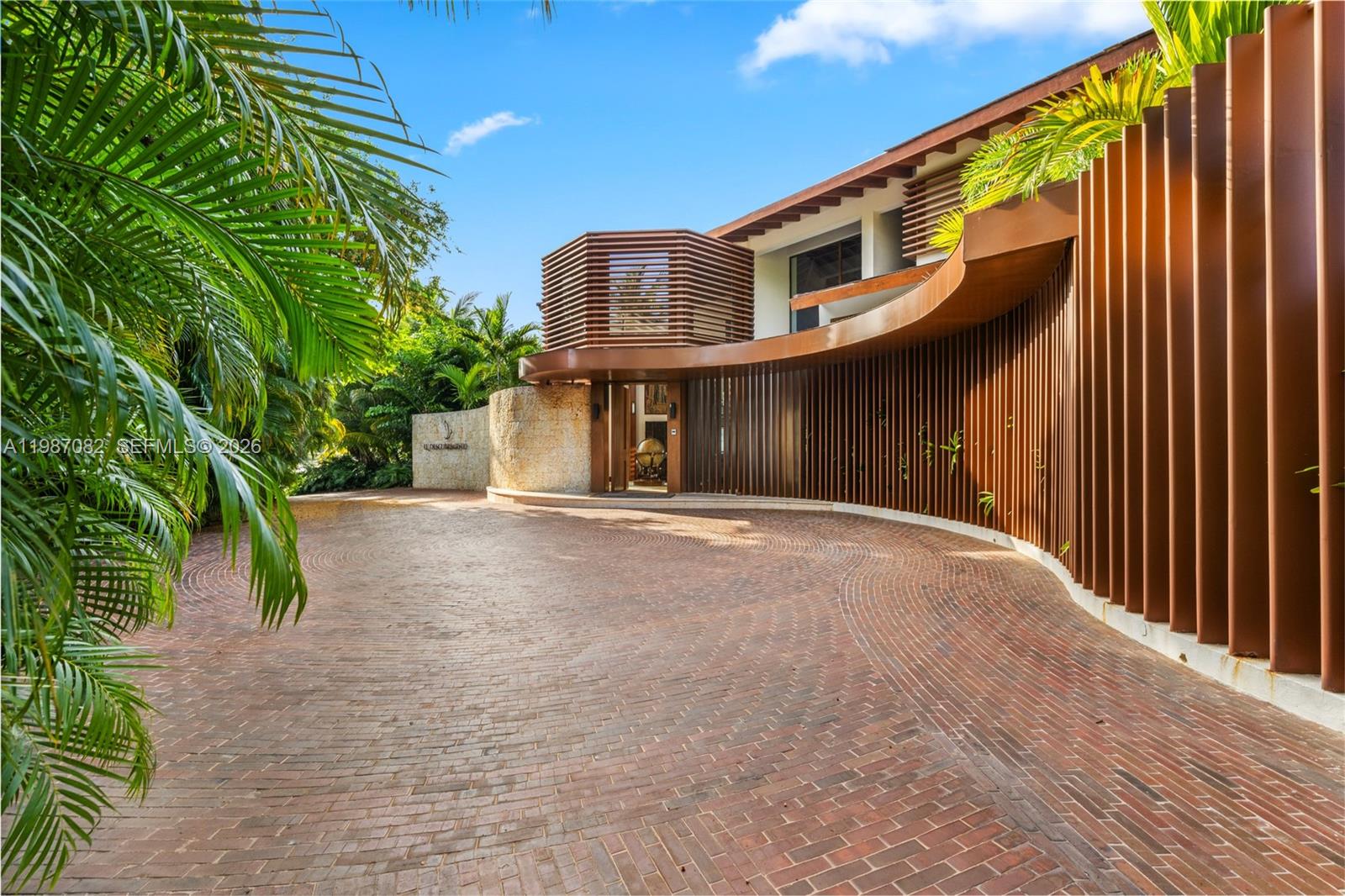 A curved brick driveway leads to a modern house entrance with vertical bronze-colored metal slats — Las Palmas 21 A Casa de Campo, La Romana, Dominic, FL