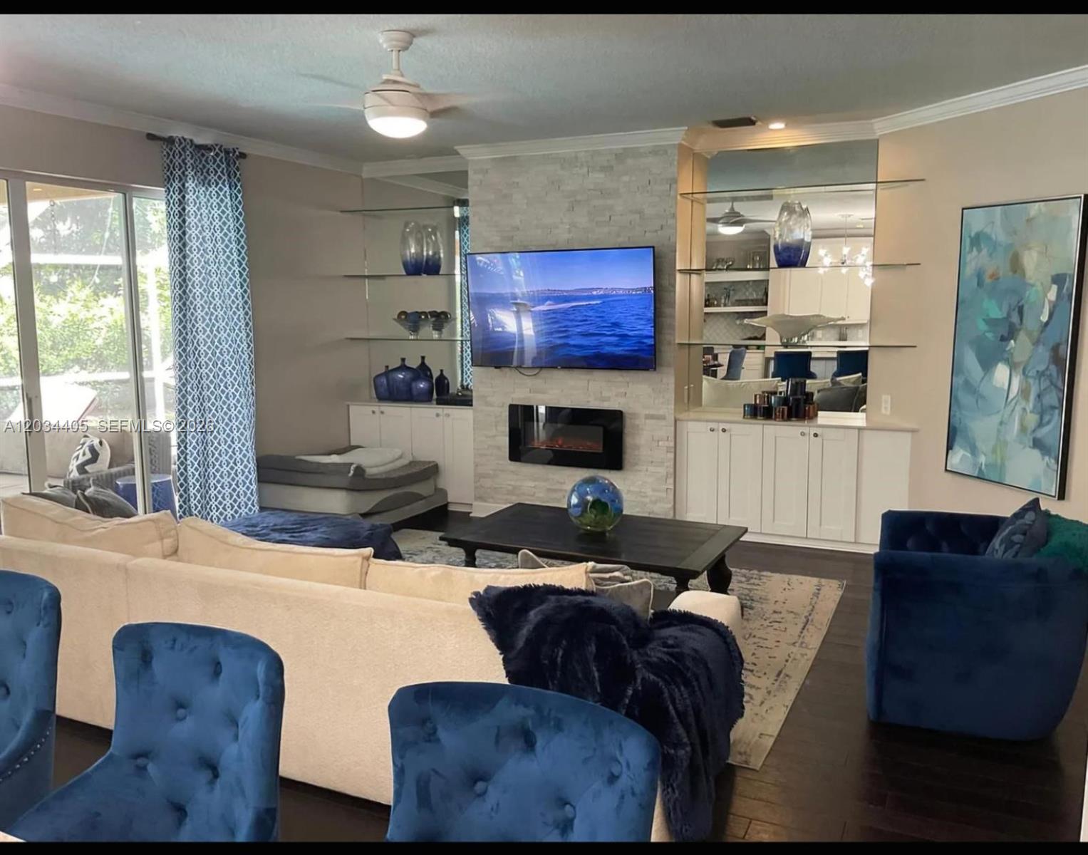 A living room features a stone fireplace, wall-mounted television, built-in shelving, and blue velvet furniture — 8682 Via Ancho Rd # 0, Boca Raton FL 33433, BOCA RATON, FL