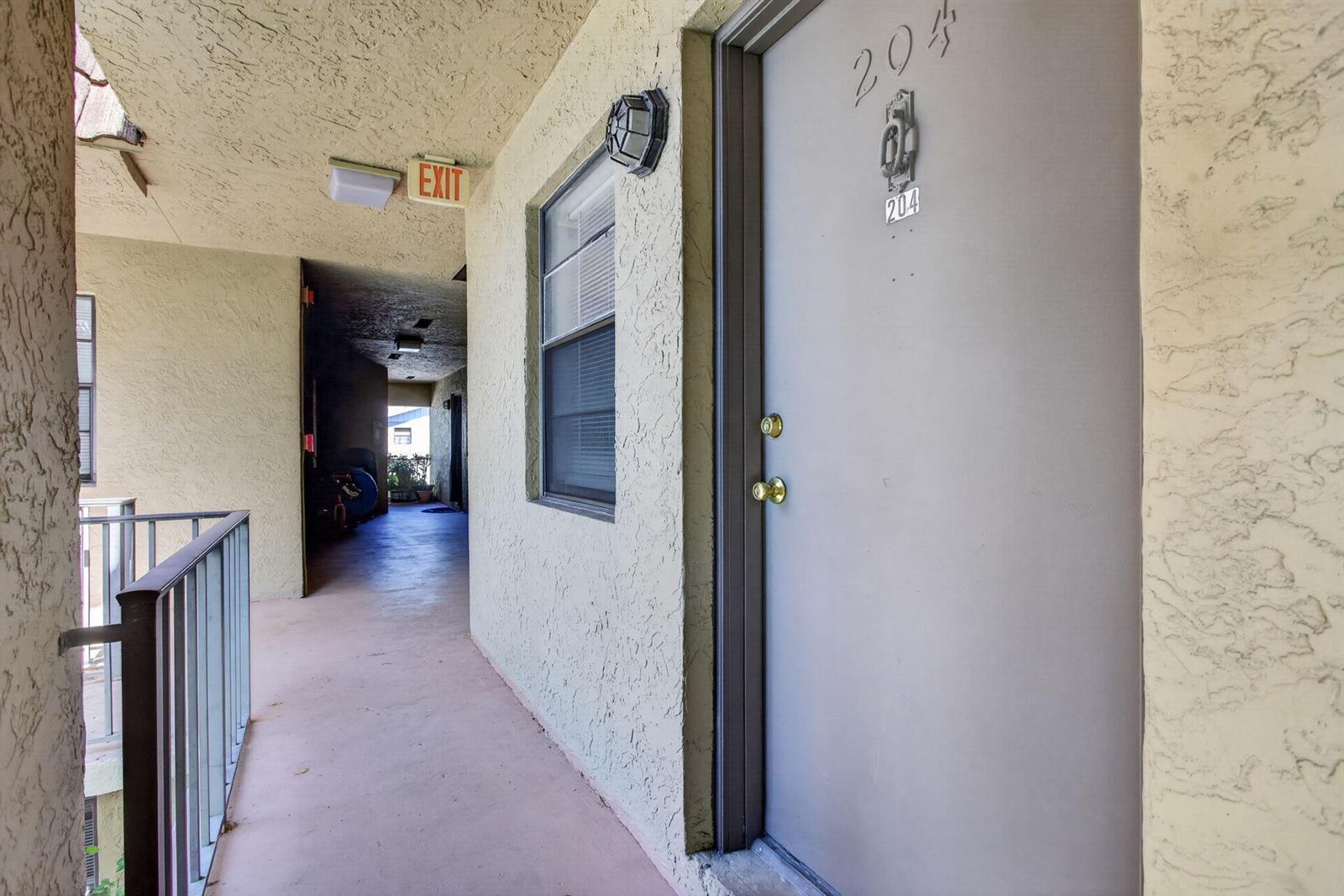 An exterior view of an apartment hallway featuring a gray door numbered 204 — 2141 NE 42nd Street # 204, Lighthouse Point FL 33064, LIGHTHOUSE POINT, FL