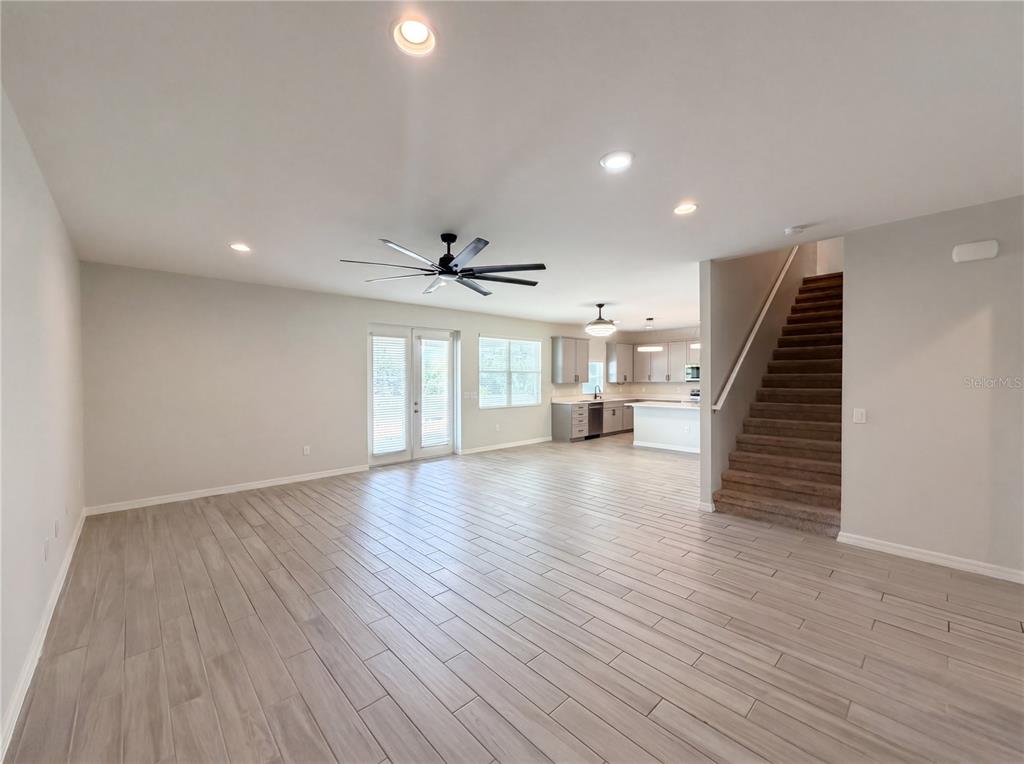 An open-concept living area features light wood-look tile flooring, a staircase, and a kitchen — 4510 PENKERT PLACE, LAKELAND, FL