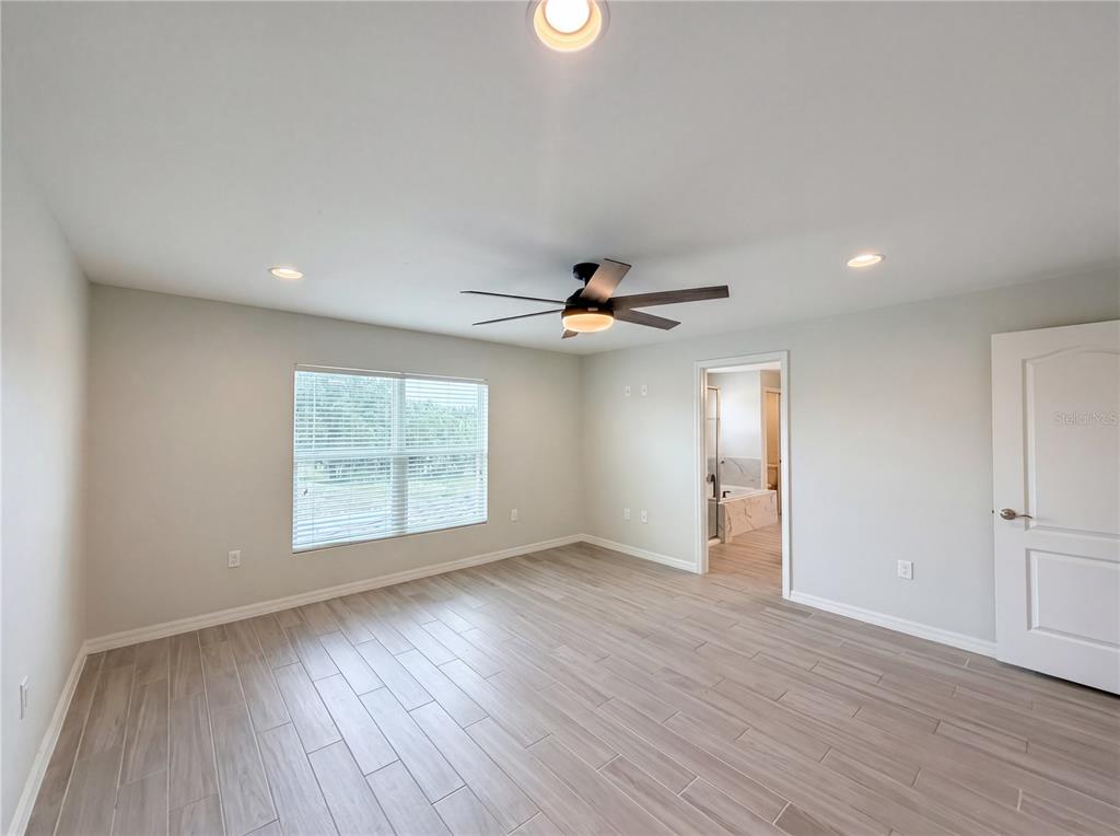 A bedroom with light gray walls, wood-look tile flooring, a ceiling fan, and an attached bathroom — 4510 PENKERT PLACE, LAKELAND, FL