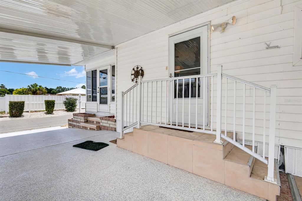 A covered carport leads to a white home with two entry doors and tiled stairs — 2107 PALMA SOLA BOULEVARD UNIT 17, BRADENTON, FL