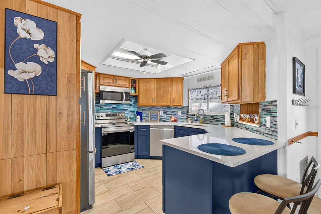 A kitchen features blue lower cabinets, wood upper cabinets, a tiled backsplash, and a breakfast bar — 2107 PALMA SOLA BOULEVARD UNIT 17, BRADENTON, FL
