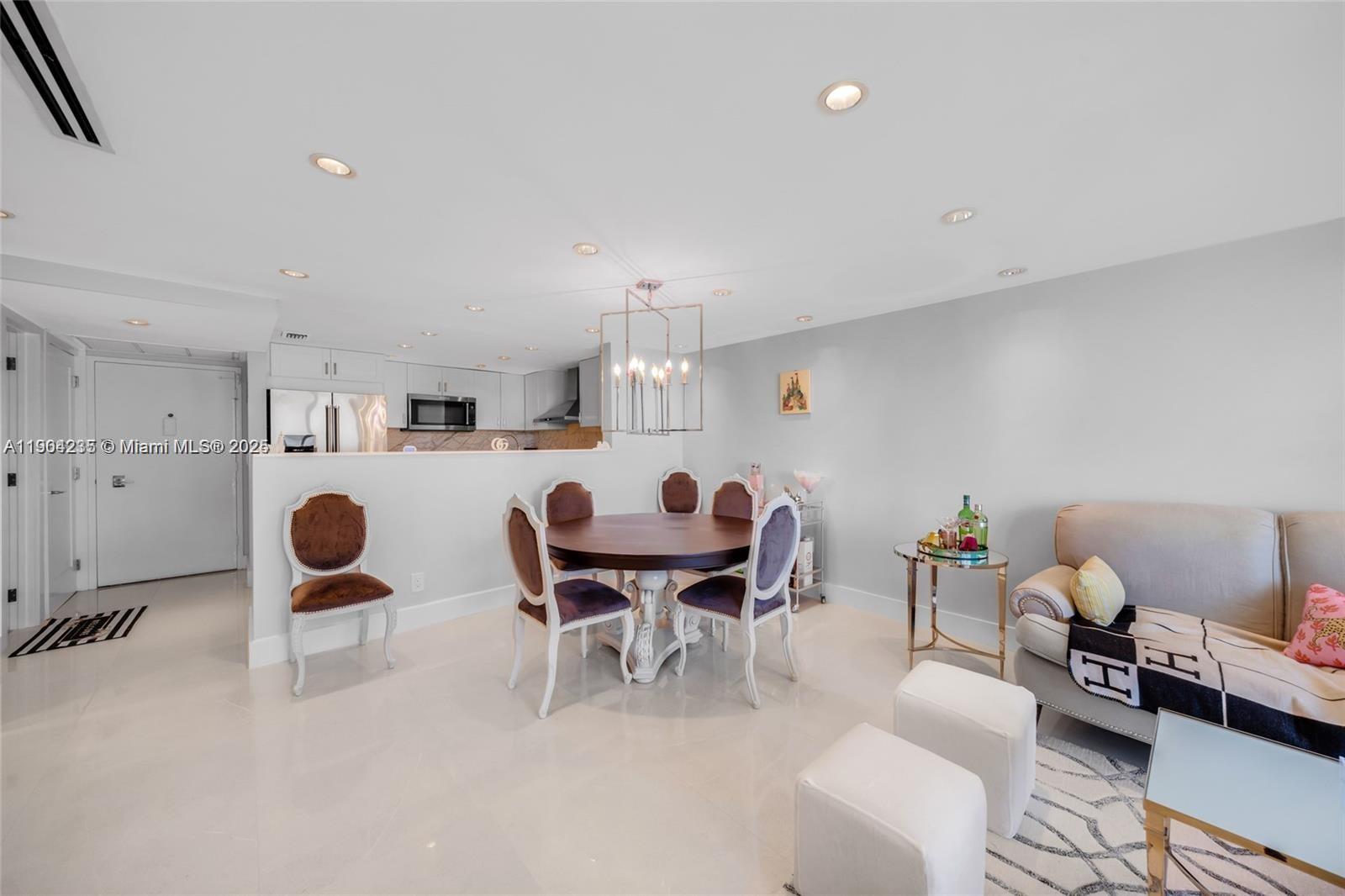 An open-concept dining and living area features a round wooden table, white tile floors, and recessed lighting — 5838 Collins Ave # 2F, Miami Beach FL 33140, MIAMI BEACH, FL