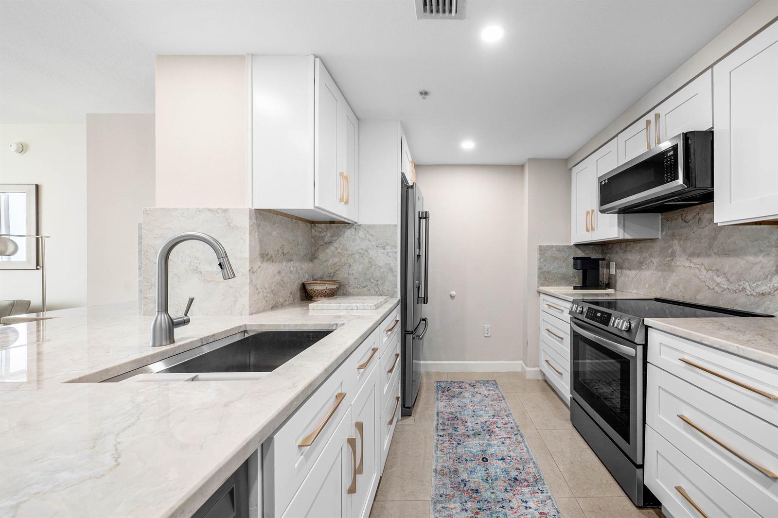 A modern kitchen features white cabinets, marble countertops, stainless steel appliances, and a patterned runner rug — 625 Casa Loma Boulevard # 1408, Boynton Beach FL 33435, BOYNTON BEACH, FL