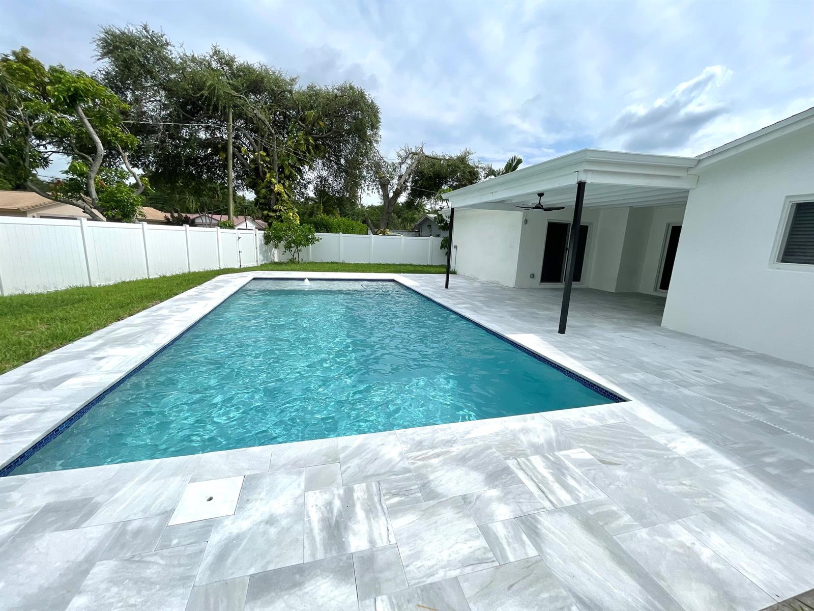 A rectangular swimming pool sits on a patio next to a white house with a pergola — 1101 NW 5th Avenue, Boca Raton FL 33432, BOCA RATON, FL