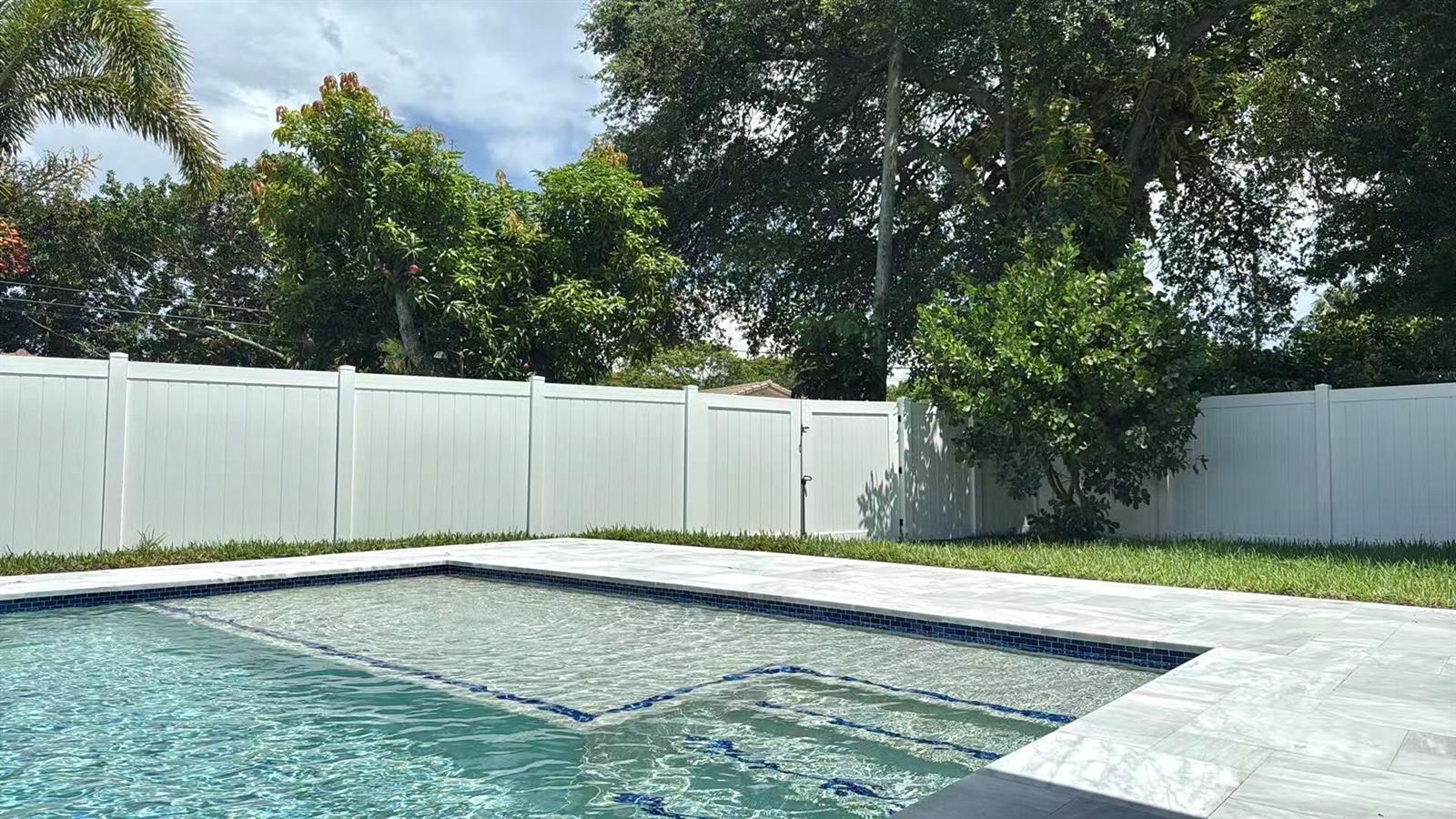 A swimming pool with a tanning ledge and blue tile accents sits before a white fence — 1101 NW 5th Avenue, Boca Raton FL 33432, BOCA RATON, FL