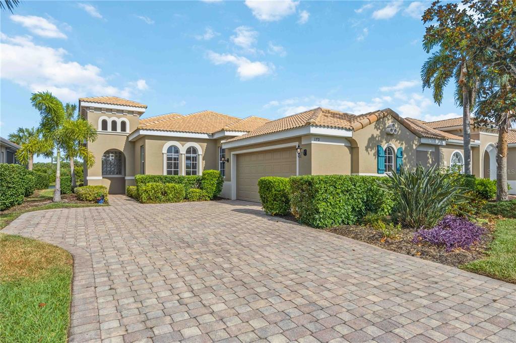 A tan stucco house with a tiled roof and a paved driveway under a blue sky — 170 CIPRIANI WAY, NORTH VENICE, FL