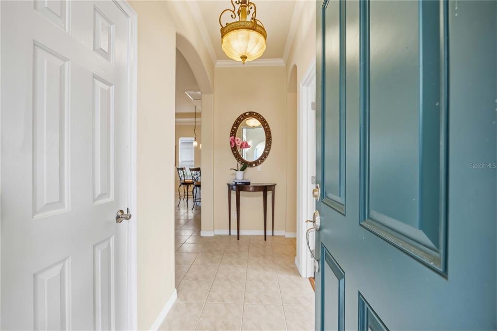 A view from an open teal front door into a tiled foyer with a chandelier — 170 CIPRIANI WAY, NORTH VENICE, FL