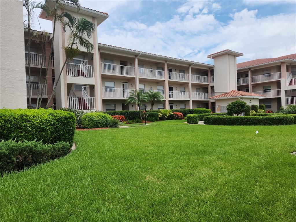 A three-story apartment building with balconies overlooks a manicured lawn and landscaped hedges — 6507 STONE RIVER ROAD UNIT 205, BRADENTON, FL