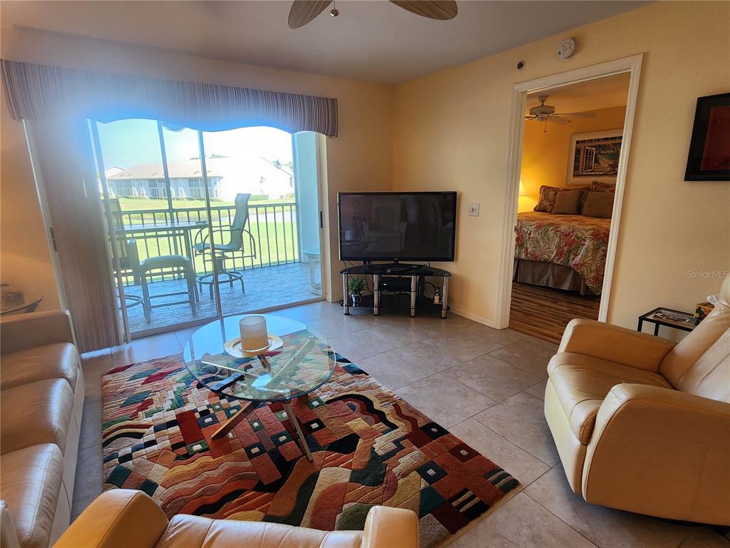A living room features a patterned area rug, glass coffee table, television, and sliding glass doors — 6507 STONE RIVER ROAD UNIT 205, BRADENTON, FL