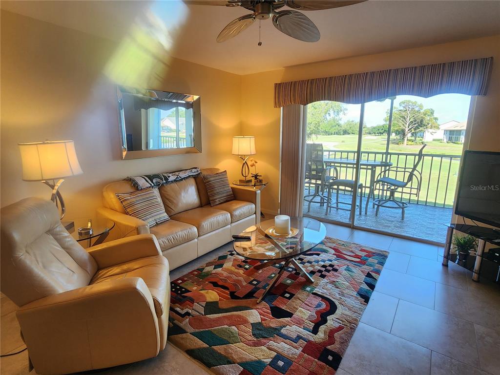 A living room features a leather sofa, armchair, patterned rug, and a balcony with golf views — 6507 STONE RIVER ROAD UNIT 205, BRADENTON, FL