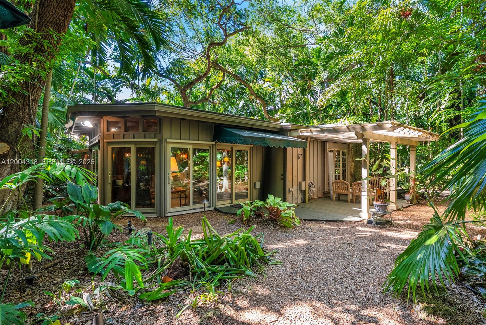 A single-story house with a wooden deck and pergola sits in a lush, wooded area — 3584 Saint Gaudens Rd, Miami FL 33133, MIAMI, FL