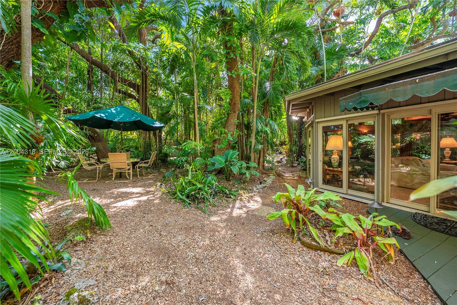 A patio area with a table and umbrella sits outside a house with glass doors — 3584 Saint Gaudens Rd, Miami FL 33133, MIAMI, FL