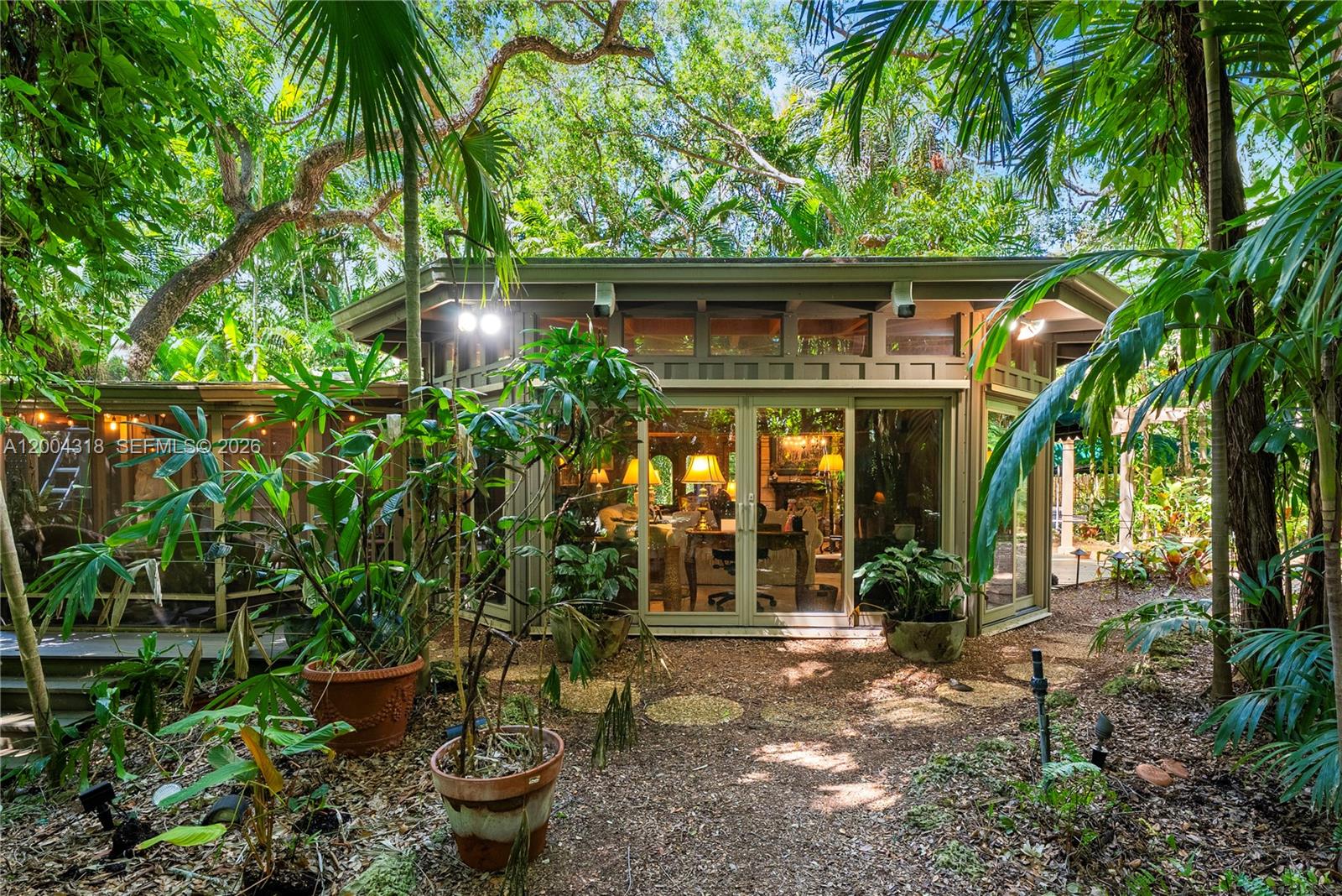 A glass-walled structure sits nestled in a lush, wooded garden with potted plants — 3584 Saint Gaudens Rd, Miami FL 33133, MIAMI, FL