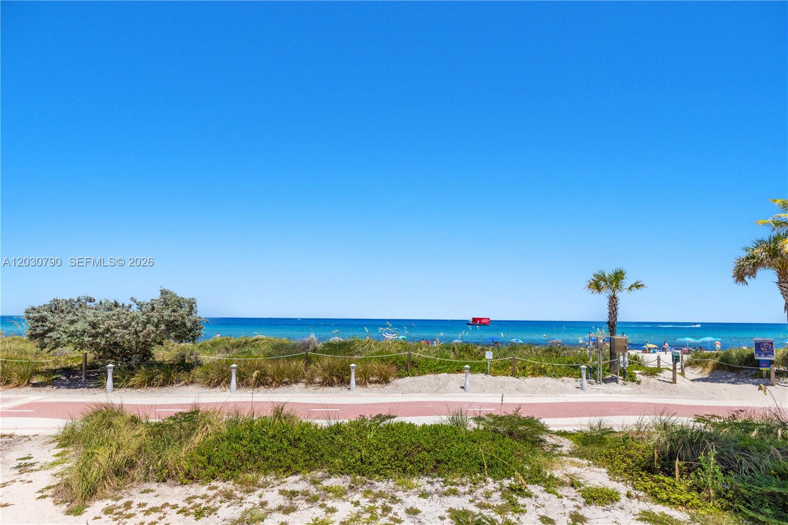 A paved path runs alongside sand dunes and vegetation leading to a sunny beach — 5445 Collins Ave # 1506, Miami Beach FL 33140, MIAMI BEACH, FL