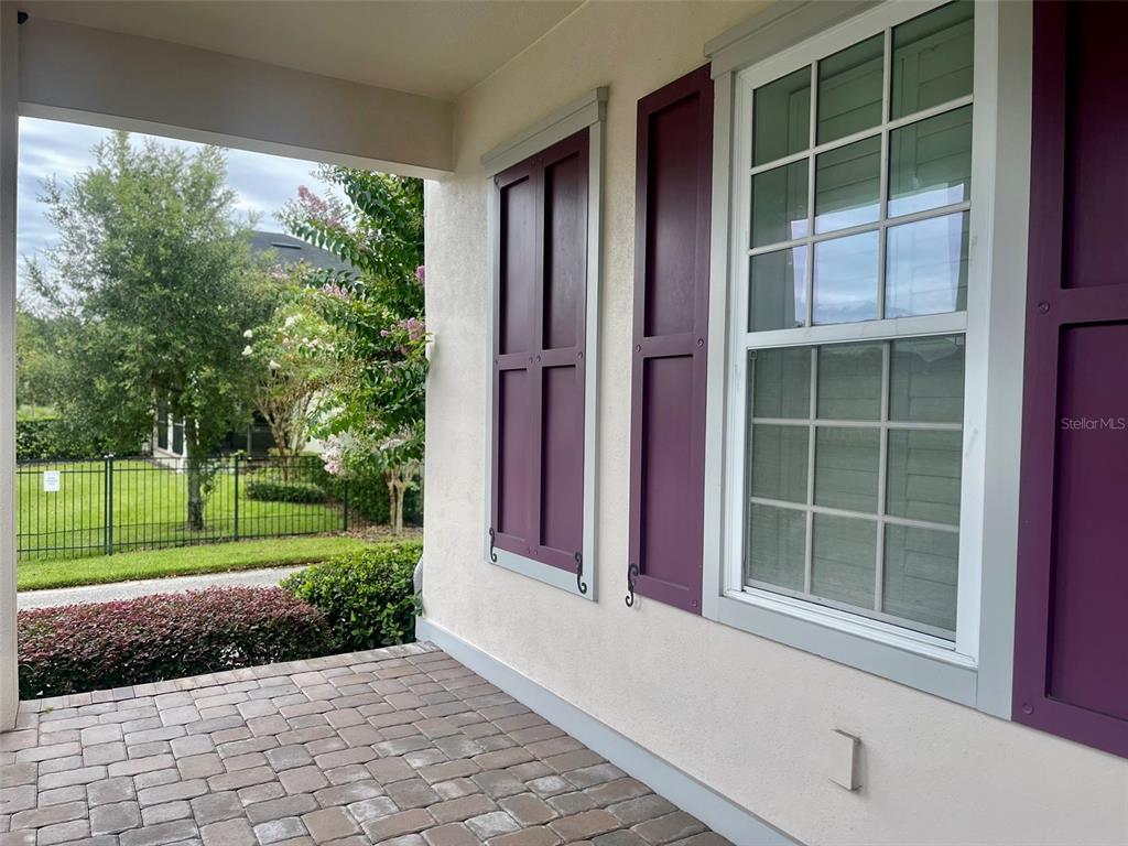 A covered porch features brick pavers, light stucco walls, and windows with purple shutters — 13892 HEANEY AVENUE, ORLANDO, FL
