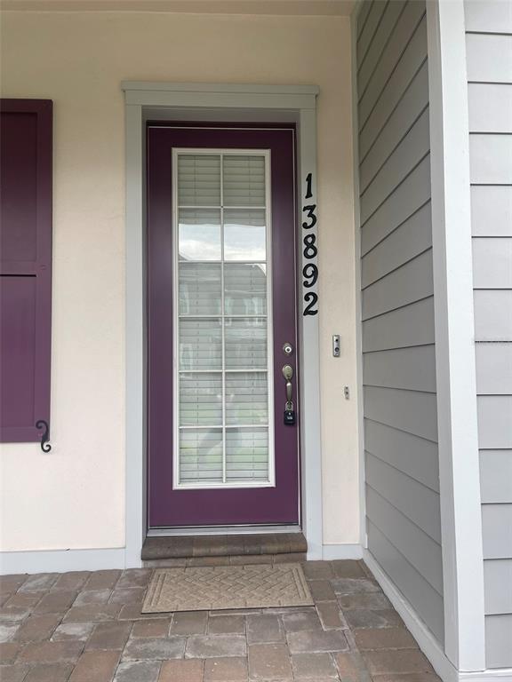 A purple front door with a glass pane and vertical house numbers sits on a porch — 13892 HEANEY AVENUE, ORLANDO, FL