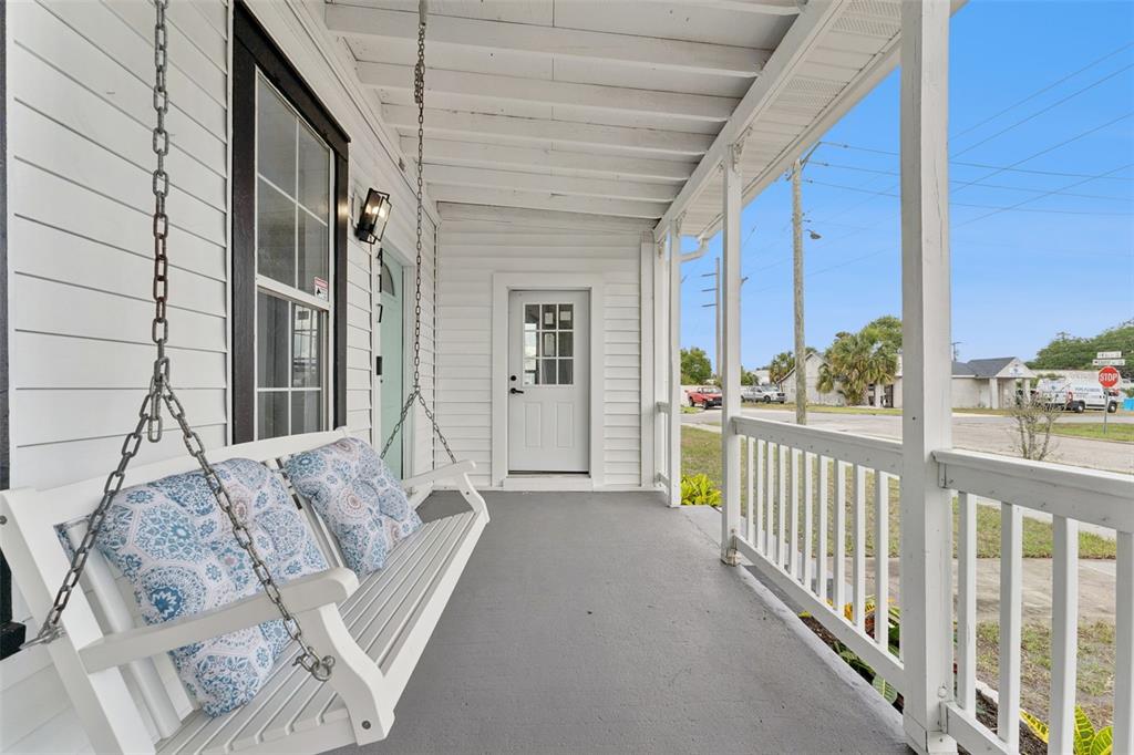 A white porch features a hanging swing, gray flooring, and a white front door — 417 W 6TH STREET, SANFORD, FL