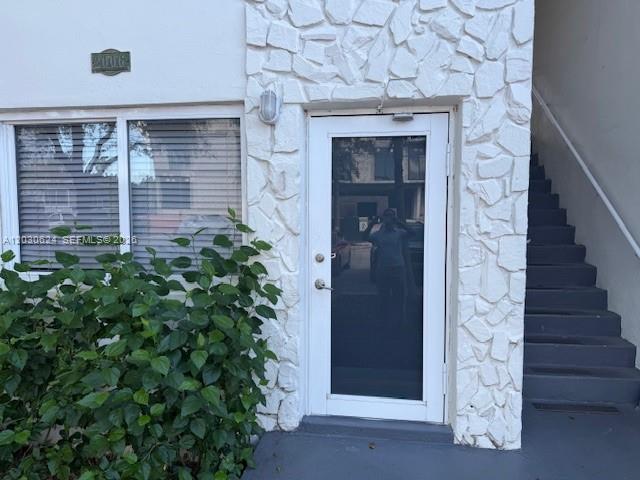 A white building exterior features a stone-textured facade, a glass-paneled door, and adjacent stairs — 2006 Calais Dr # 1, Miami Beach FL 33141, MIAMI BEACH, FL