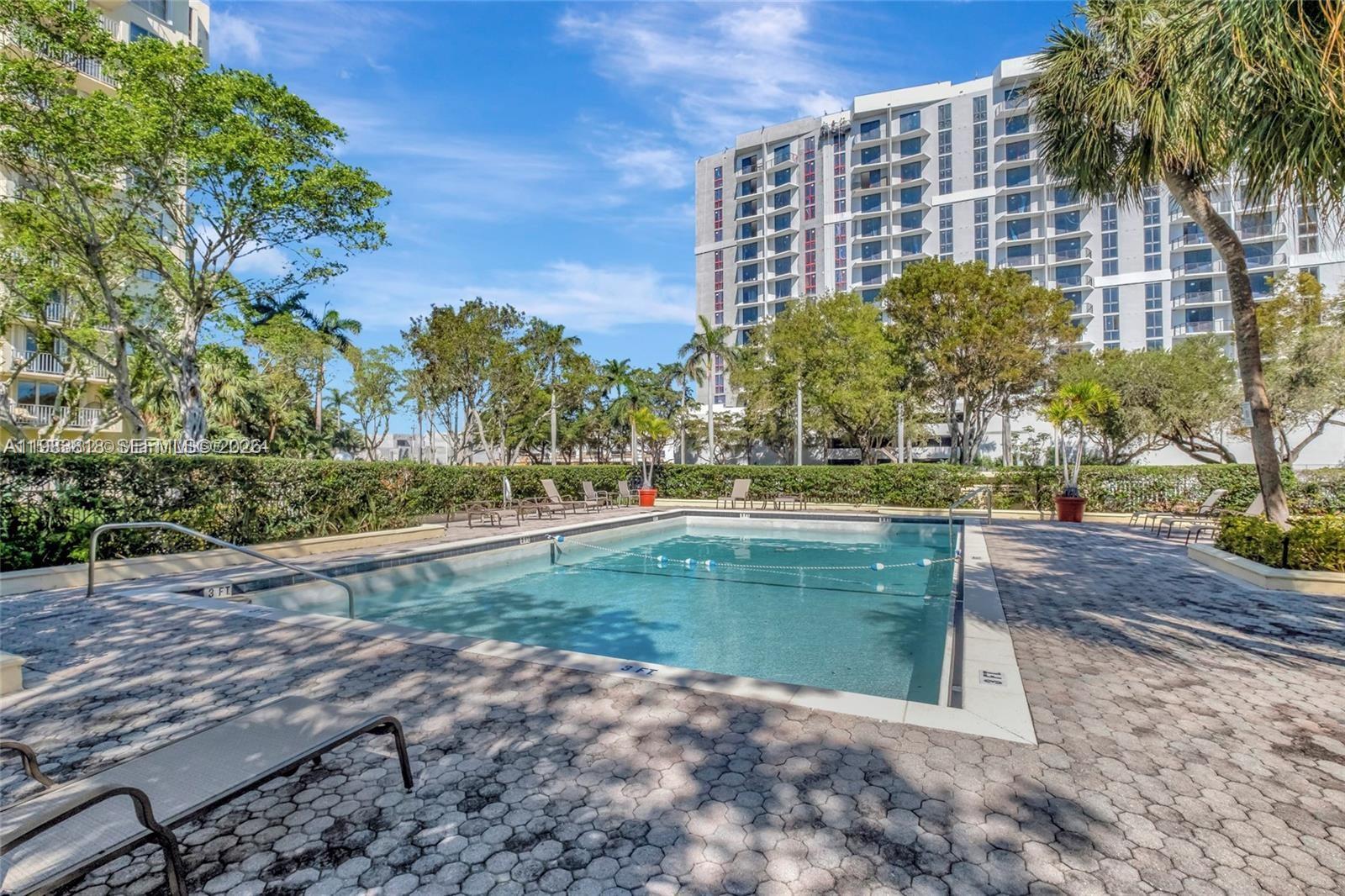 A rectangular swimming pool sits on a paved deck surrounded by trees and a building — 11111 Biscayne Blvd # 8F, Miami FL 33181, MIAMI, FL