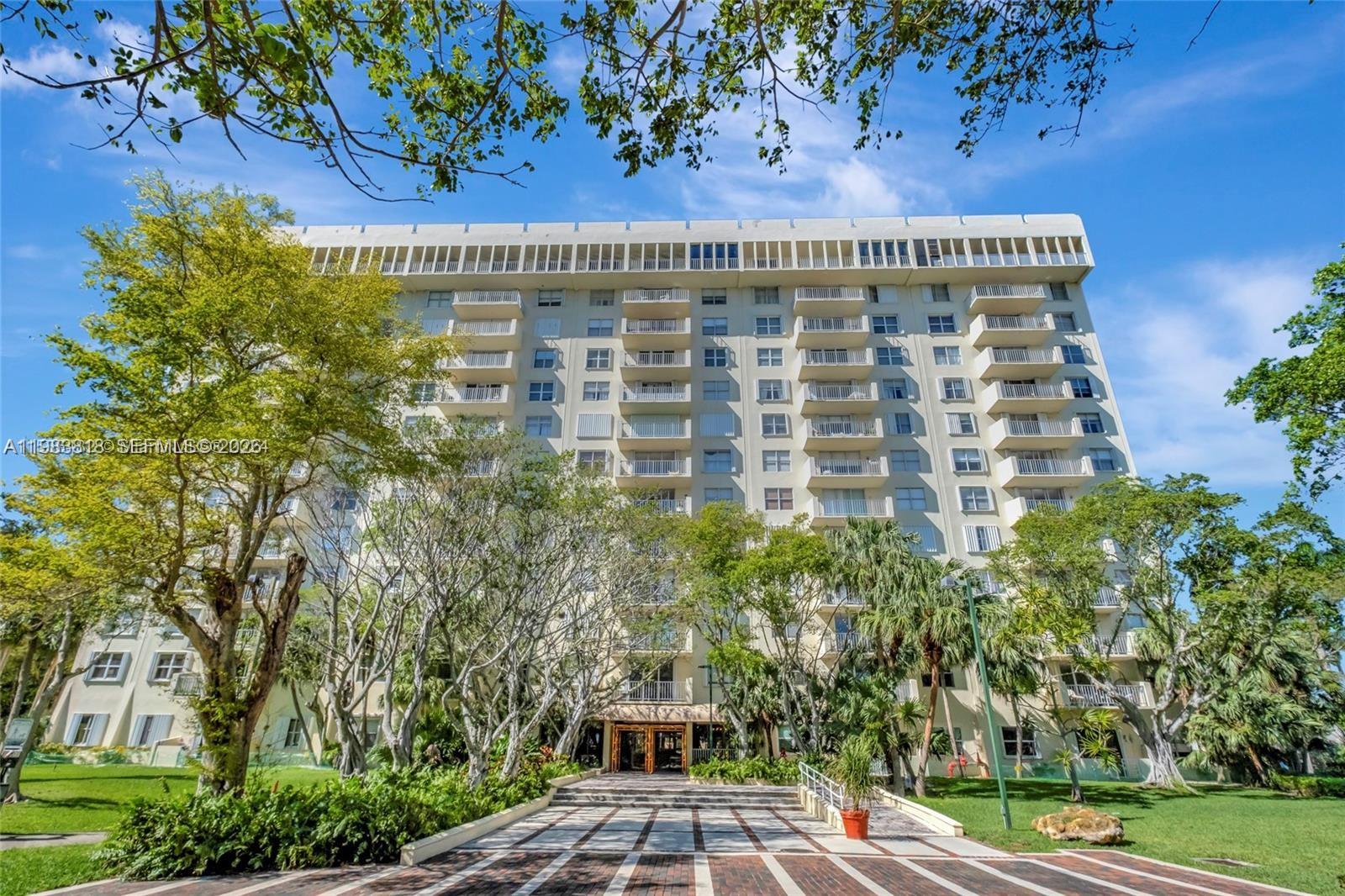 A multi-story residential building features balconies and a paved entrance surrounded by mature trees — 11111 Biscayne Blvd # 8F, Miami FL 33181, MIAMI, FL