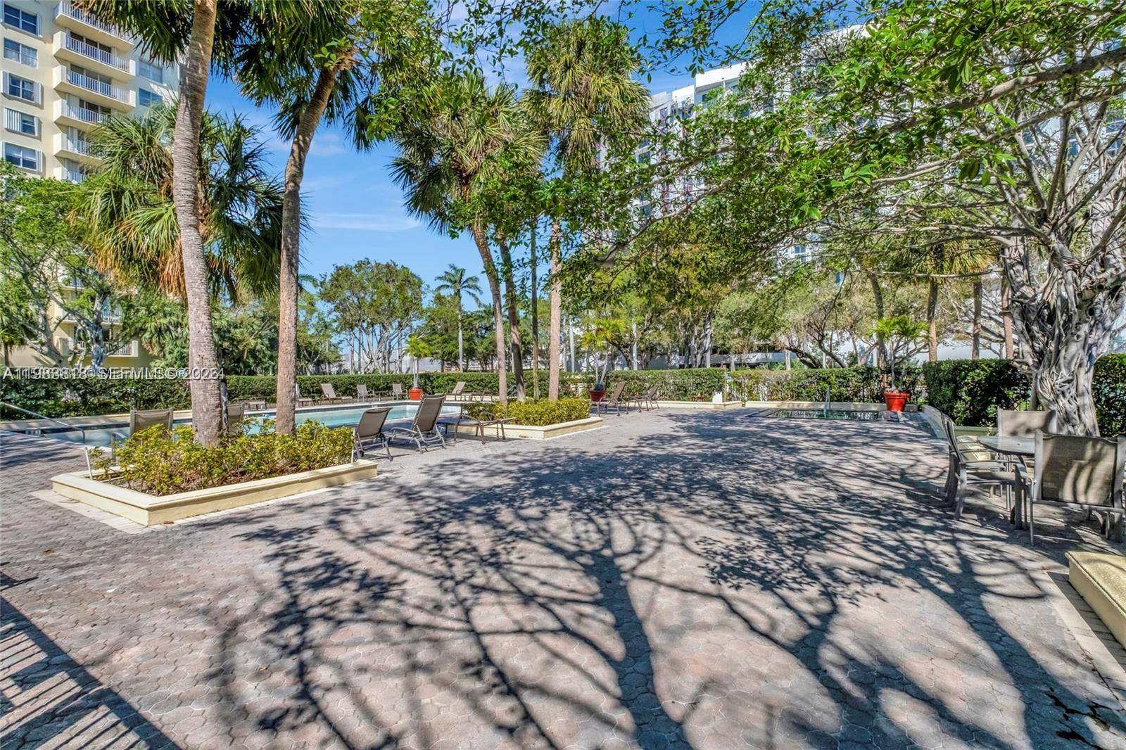 A paved outdoor patio area features lounge chairs, palm trees, and a swimming pool — 11111 Biscayne Blvd # 8F, Miami FL 33181, MIAMI, FL