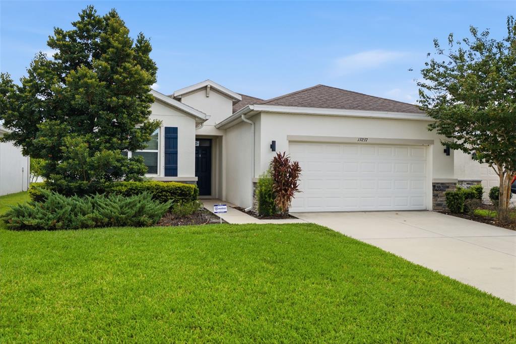 A single-story house with a white stucco exterior, a two-car garage, and a front lawn — 13237 WATERLEAF GARDEN CIRCLE, RIVERVIEW, FL