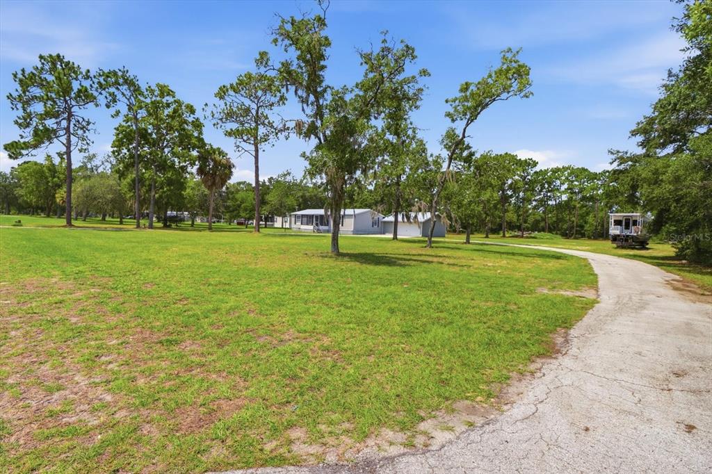 A grassy yard with scattered trees leads to a house and a detached garage — 7230 S SONATA AVENUE, HOMOSASSA, FL