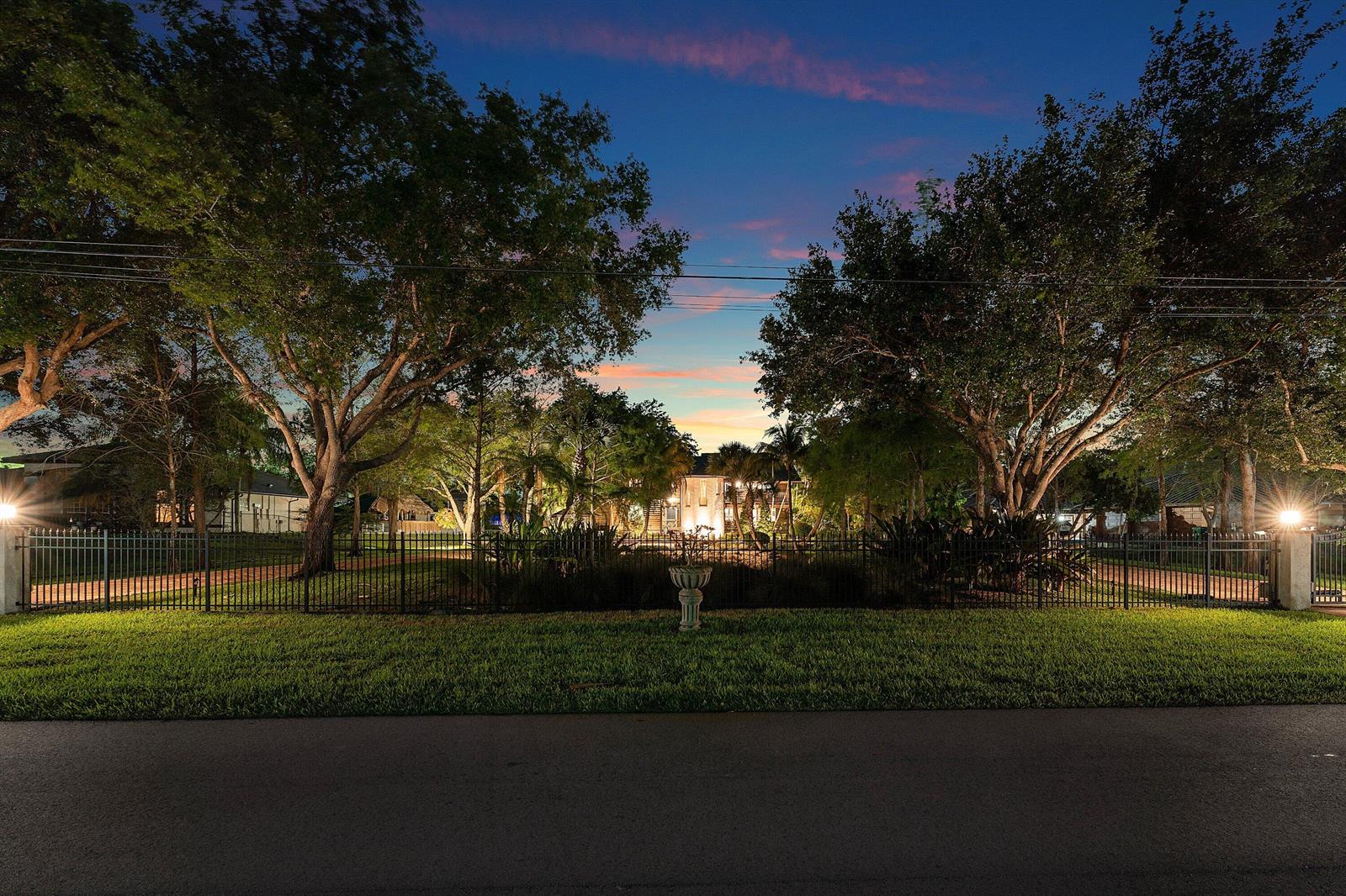A house is visible behind a black metal fence and trees at twilight — 6002 NW 74th Terrace, Parkland FL 33067, PARKLAND, FL
