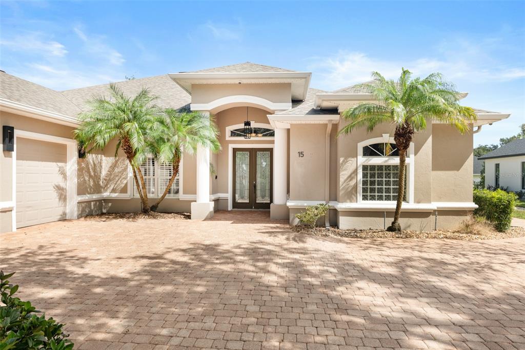A beige single-story house features a paver driveway, double front doors, and two palm trees — 15 OLD OAK DRIVE N, PALM COAST, FL