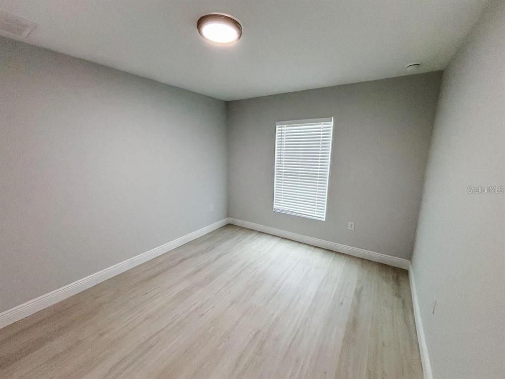 An empty room features light gray walls, wood-look flooring, and a single window with blinds — 13257 BLYTHEVILLE AVENUE UNIT 13259, PORT CHARLOTTE, FL