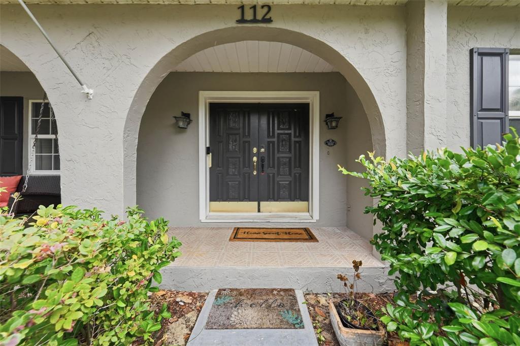 The exterior view shows a covered entryway with a double door and arched stucco ceiling — 112 E GARDENIA STREET, HOWEY IN THE HILLS, FL