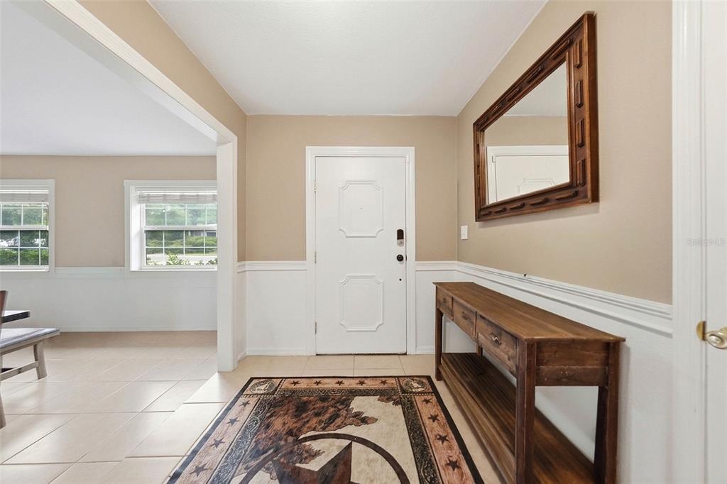 An entryway features a white door, a wooden console table, a mirror, and a rug — 112 E GARDENIA STREET, HOWEY IN THE HILLS, FL