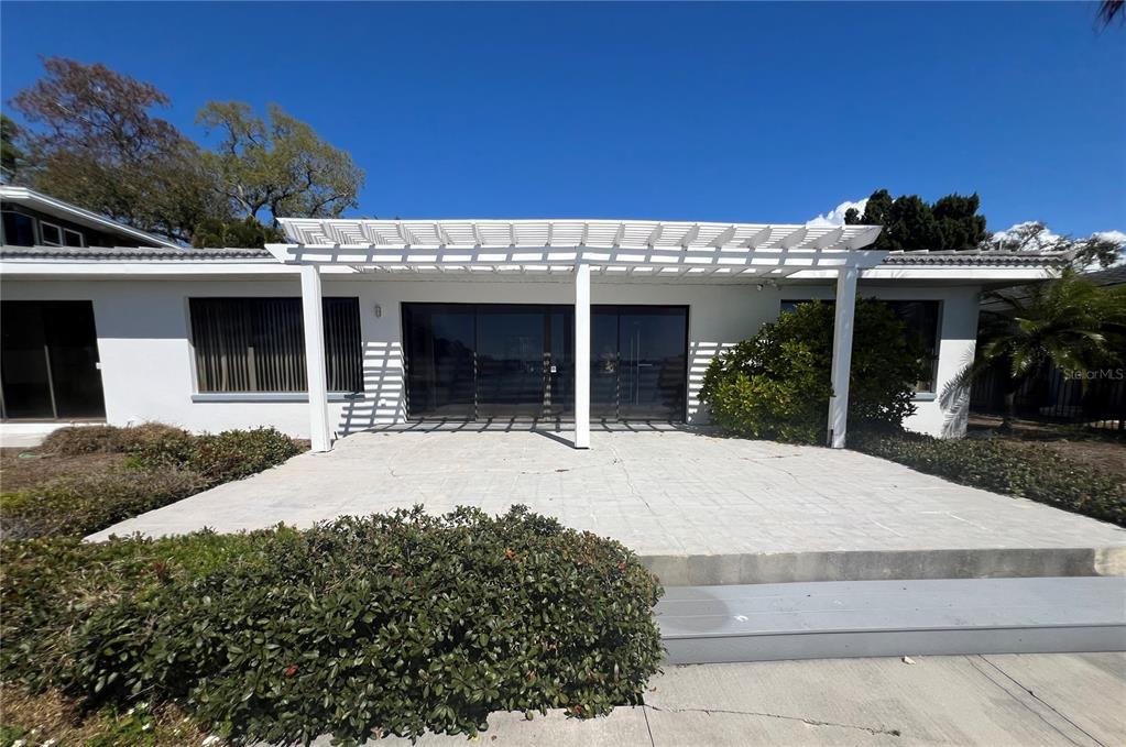 A white house features a paved patio covered by a white wooden pergola — 2431 SUNRISE DRIVE SE, ST PETERSBURG, FL