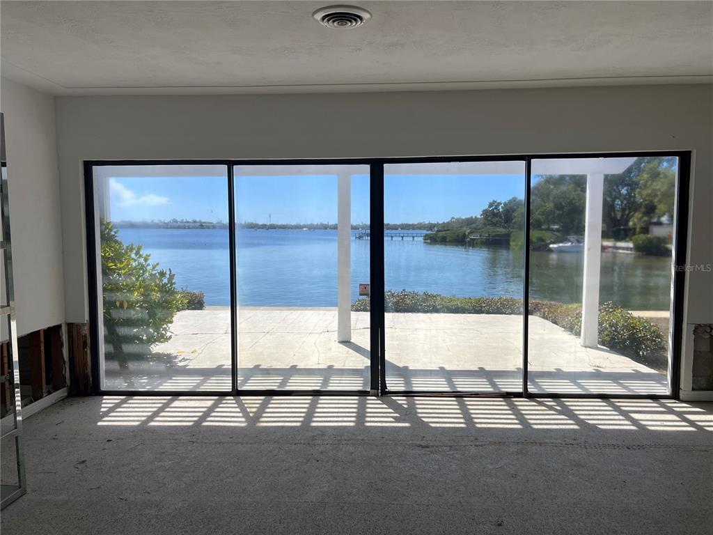 An unfinished room features large sliding glass doors overlooking a waterfront patio and bay — 2431 SUNRISE DRIVE SE, ST PETERSBURG, FL