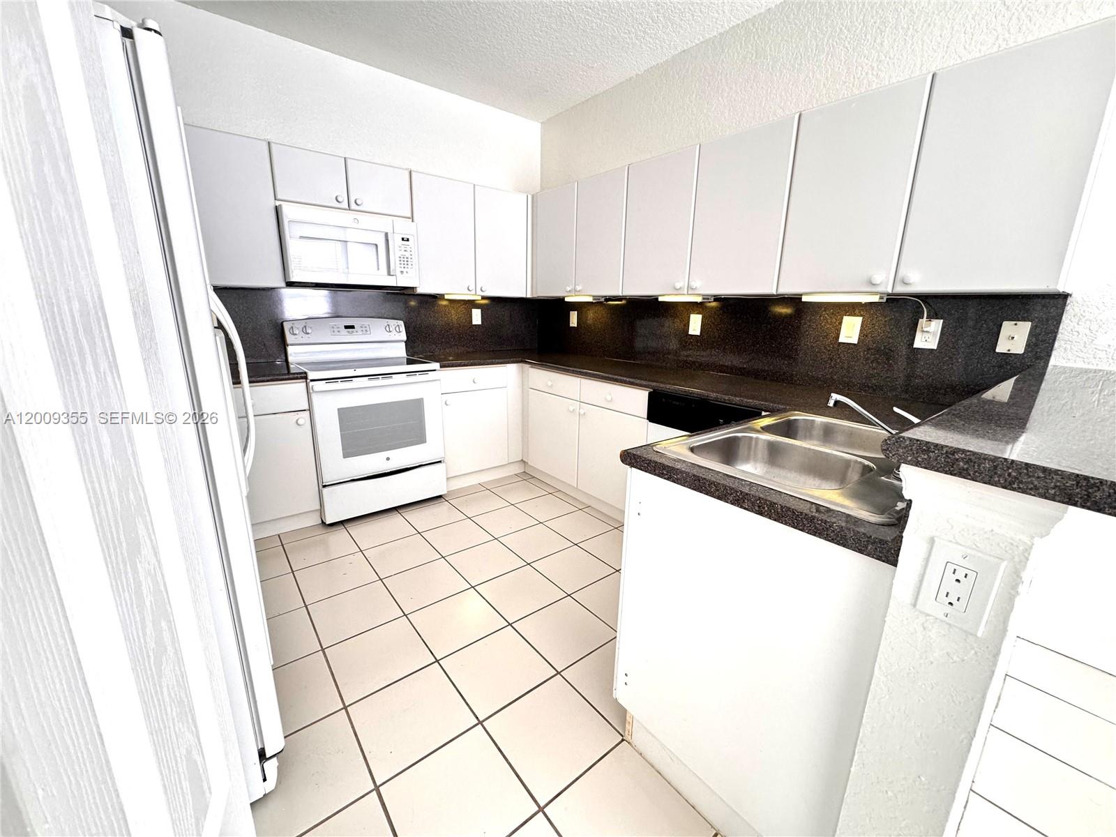 A kitchen features white cabinets, dark countertops, a white stove, and light-colored floor tiles — 4435 SW 160th Ave # 214, Miramar FL 33027, MIRAMAR, FL