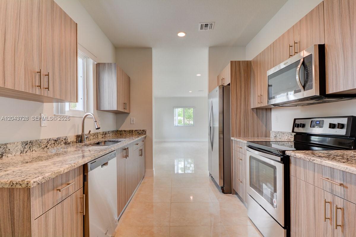 A galley kitchen features wood-grain cabinets, granite countertops, and stainless steel appliances — 312 Phippen Waiters Rd, Dania Beach FL 33004, DANIA BEACH, FL