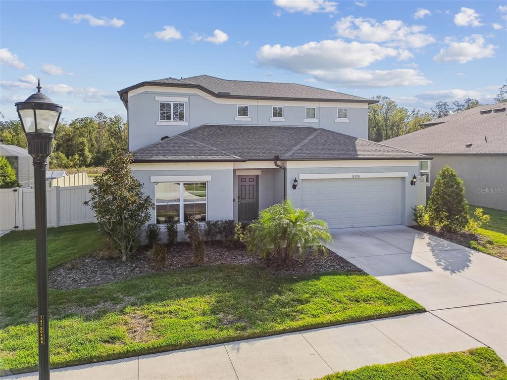 A two-story suburban house features a light gray exterior, a two-car garage, and landscaping — 18196 PORFIRIO PLACE, SPRING HILL, FL