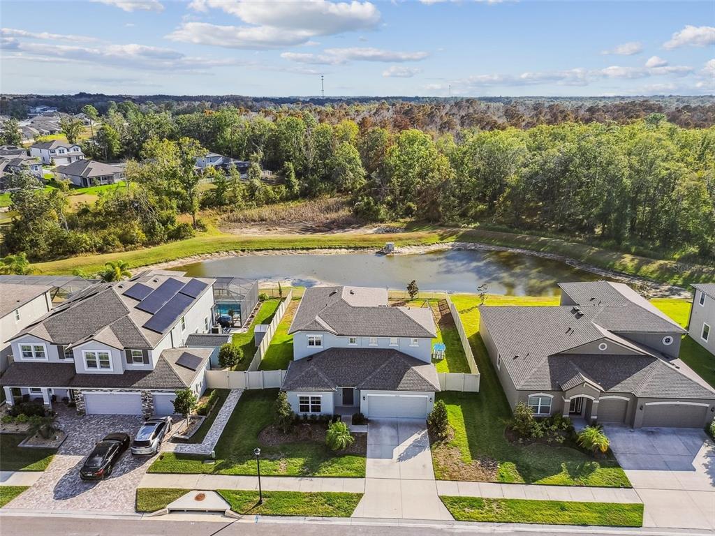 An aerial view shows three suburban houses with driveways and backyards facing a small pond — 18196 PORFIRIO PLACE, SPRING HILL, FL