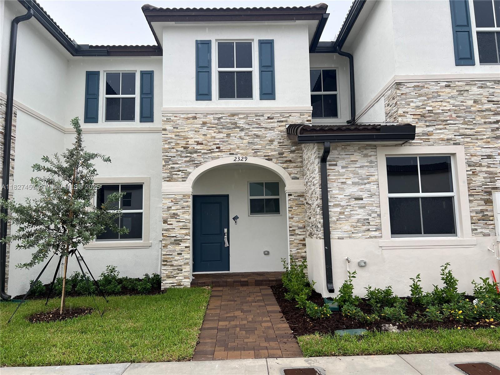 A two-story townhouse exterior features white stucco walls, stone veneer accents, and blue shutters — 2329 NW 122nd Ter, Miami FL 33167, MIAMI, FL