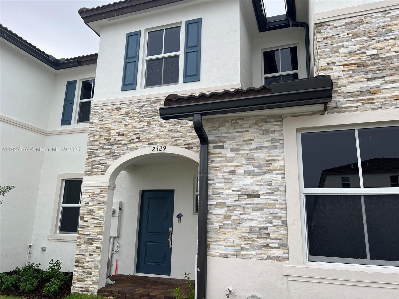 The exterior of a two-story house features stone veneer, white stucco, and a blue door — 2329 NW 122nd Ter, Miami FL 33167, MIAMI, FL