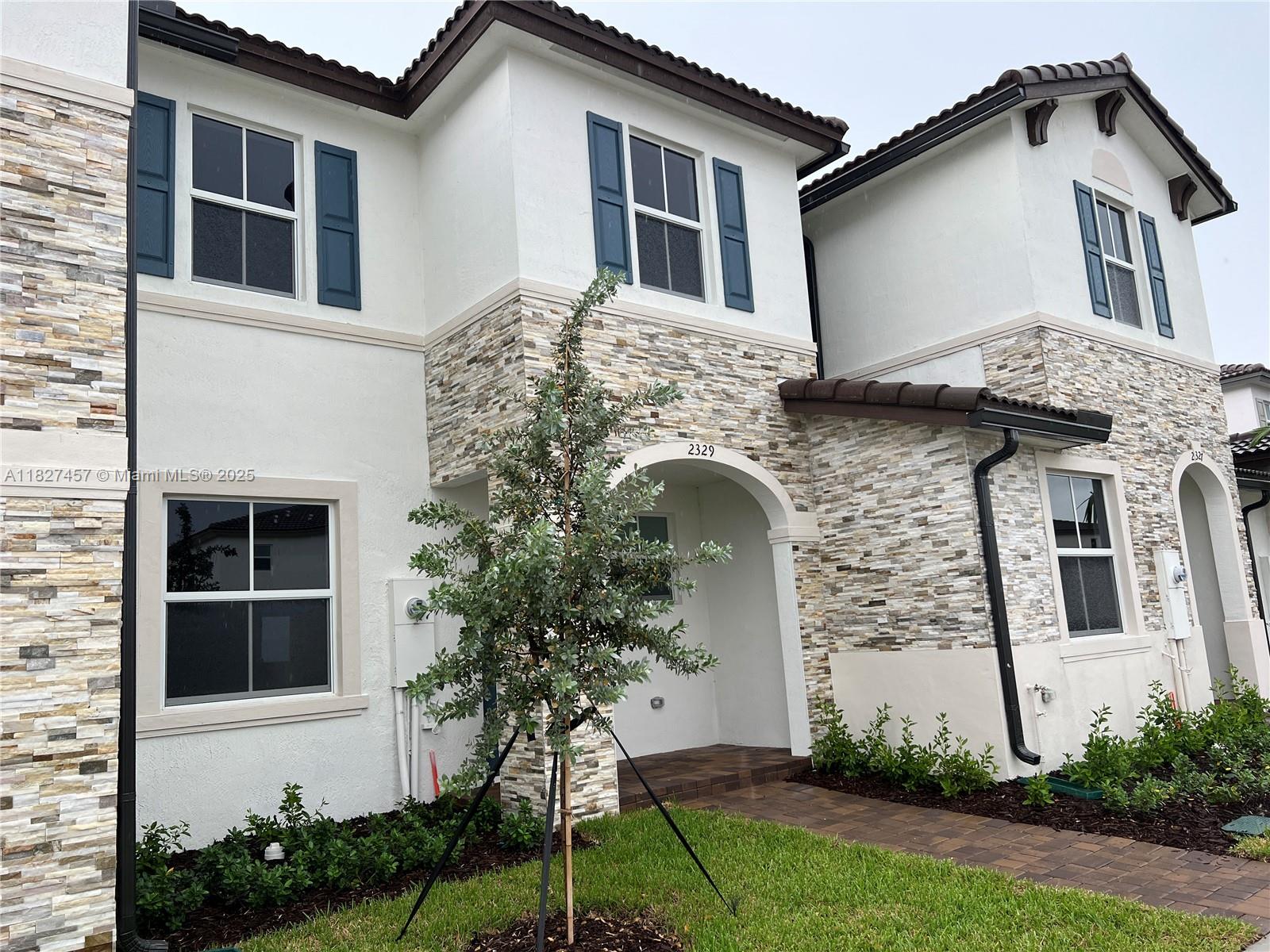 A two-story townhouse exterior features stone veneer, white stucco, blue shutters, and a paved walkway — 2329 NW 122nd Ter, Miami FL 33167, MIAMI, FL