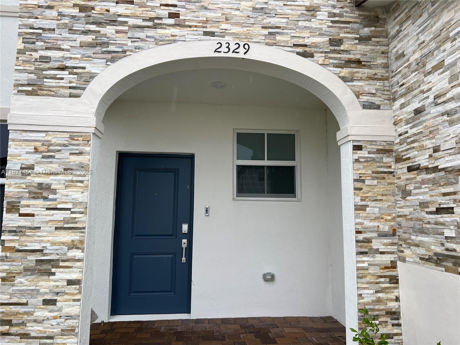 A blue front door is set within a stone-accented arched entryway — 2329 NW 122nd Ter, Miami FL 33167, MIAMI, FL