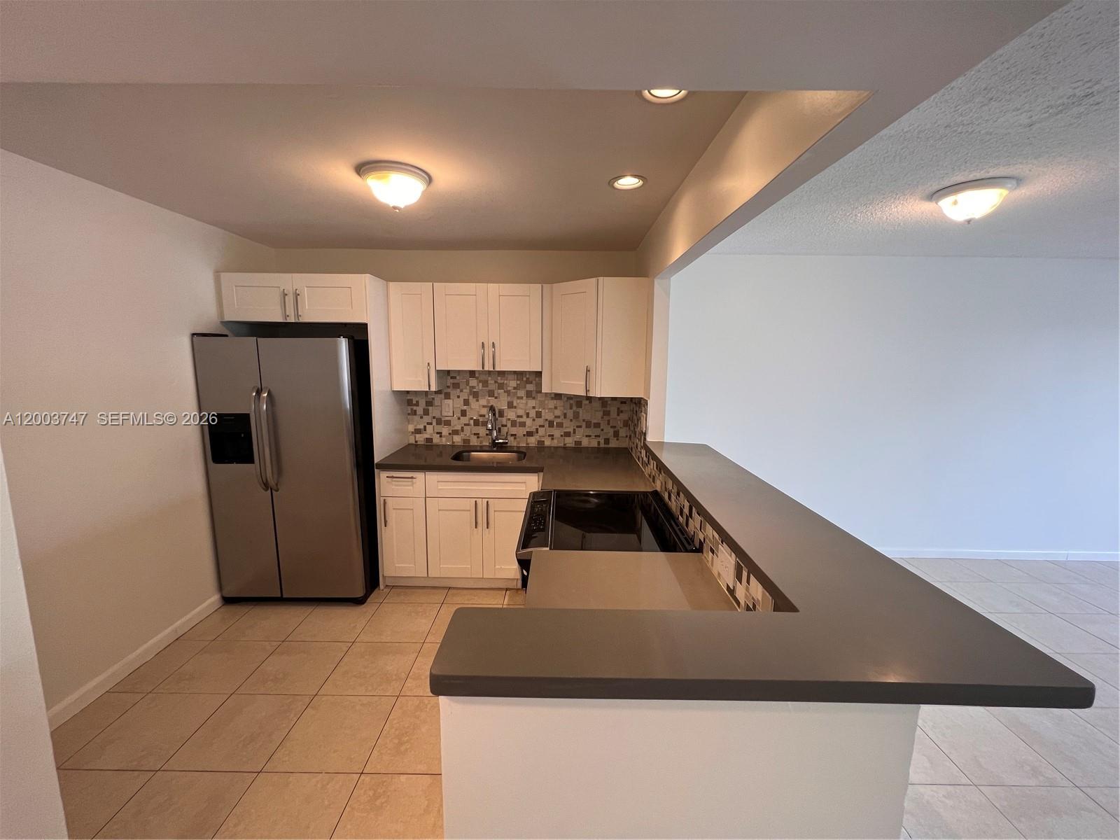 A kitchen features white cabinets, stainless steel appliances, gray countertops, and a breakfast bar — 15221 NE 6th Ave # A104, Miami FL 33162, MIAMI, FL