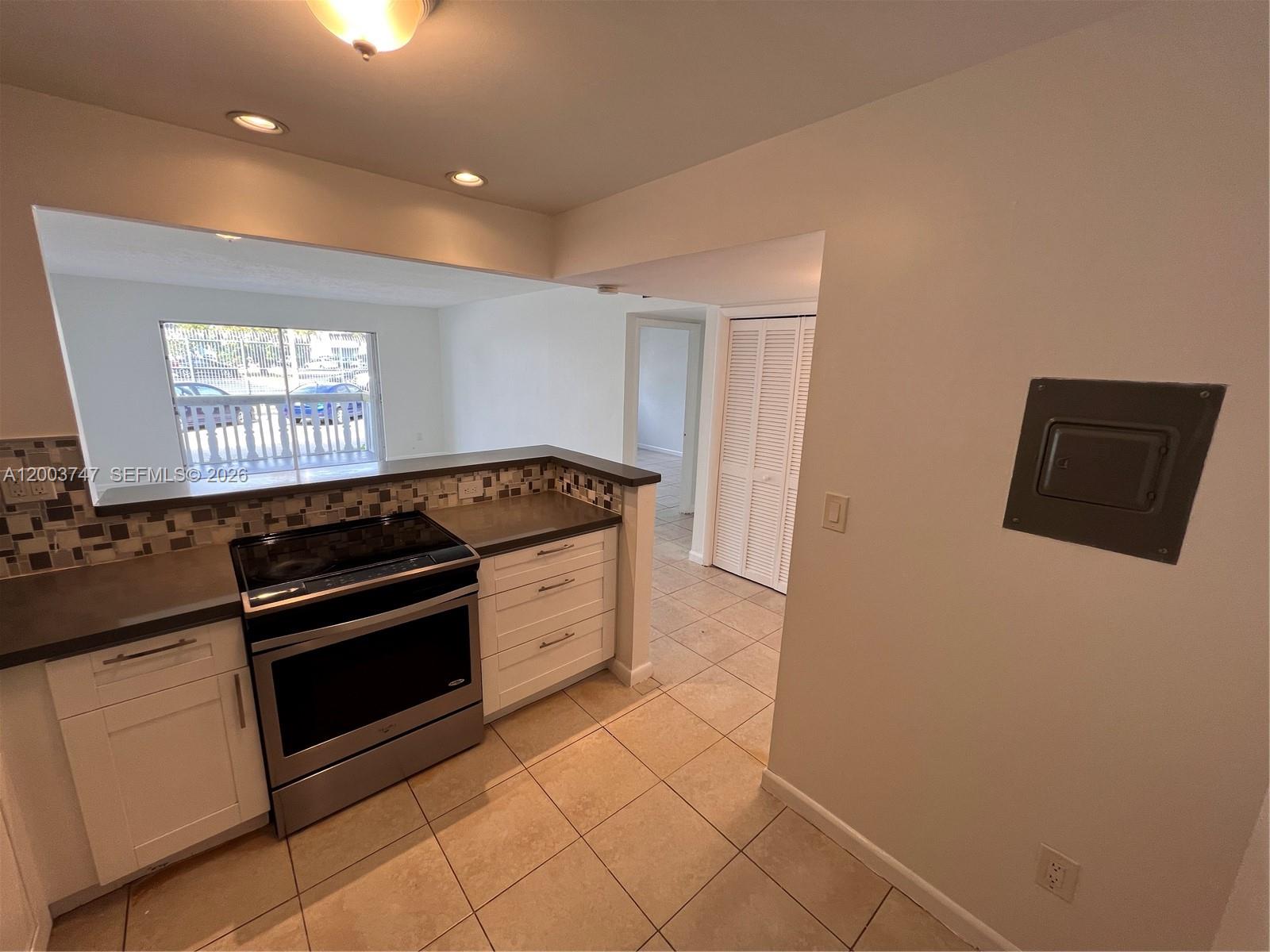 A kitchen features white cabinets, a stainless steel stove, and a pass-through to the living area — 15221 NE 6th Ave # A104, Miami FL 33162, MIAMI, FL