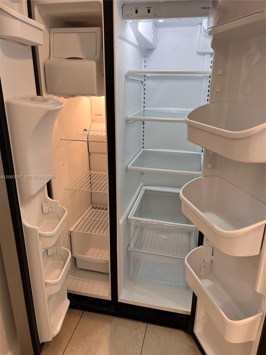 An open side-by-side refrigerator with white shelves and door bins stands on a tiled floor — 15221 NE 6th Ave # A104, Miami FL 33162, MIAMI, FL