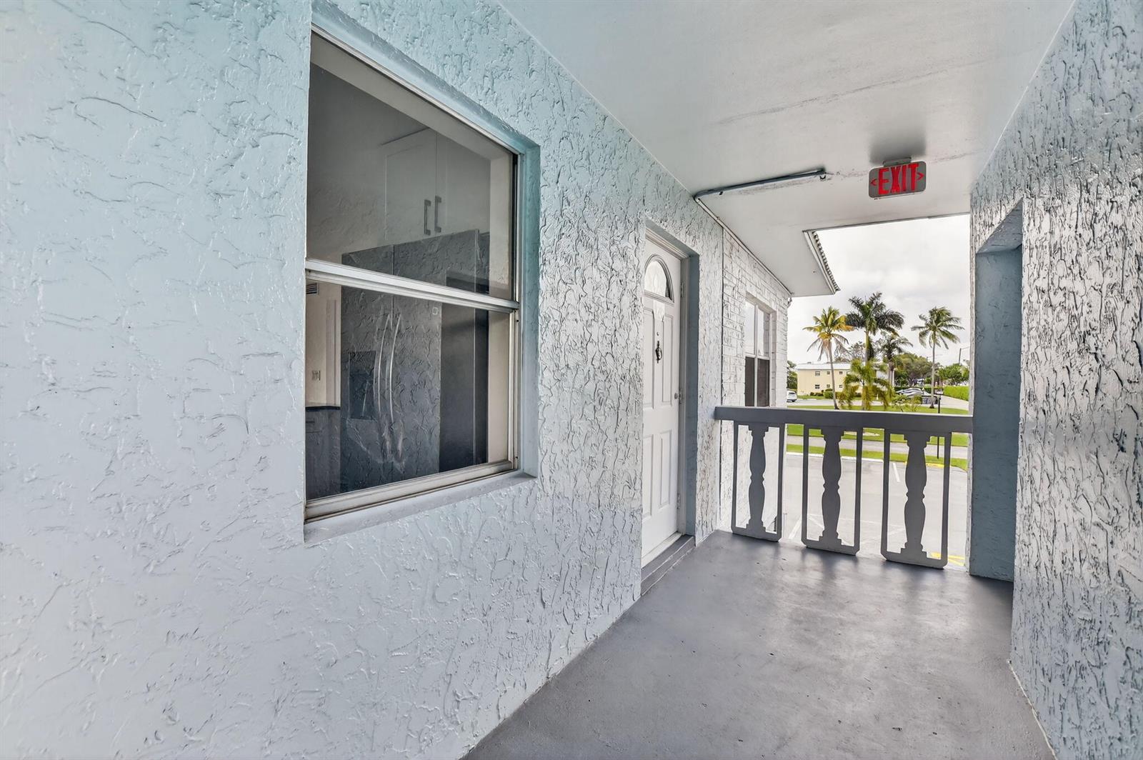 An exterior walkway with a textured light blue wall, a white door, and a balcony railing — 9780 Marina Boulevard # 425, Boca Raton FL 33428, BOCA RATON, FL