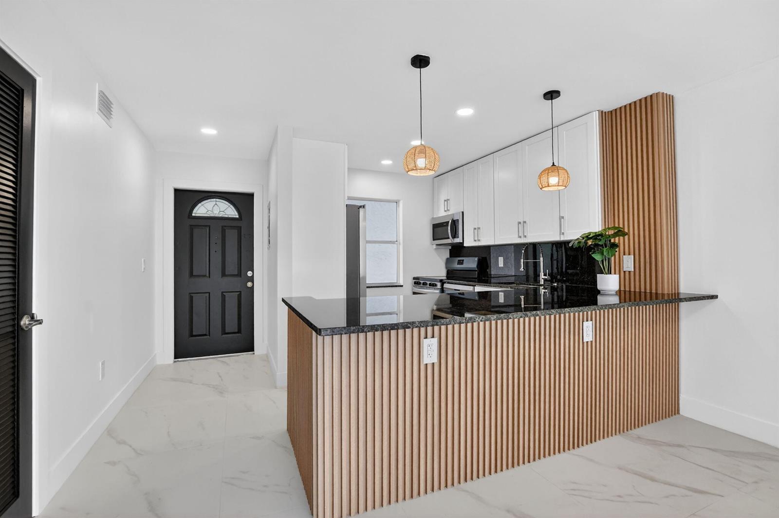 A kitchen features white cabinets, black countertops, and a wood-slatted island with pendant lighting — 9780 Marina Boulevard # 425, Boca Raton FL 33428, BOCA RATON, FL